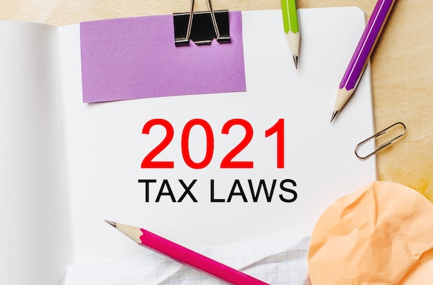 Text 2021 tax laws on a white note background with pencils, stickers and paper clips. Business concept