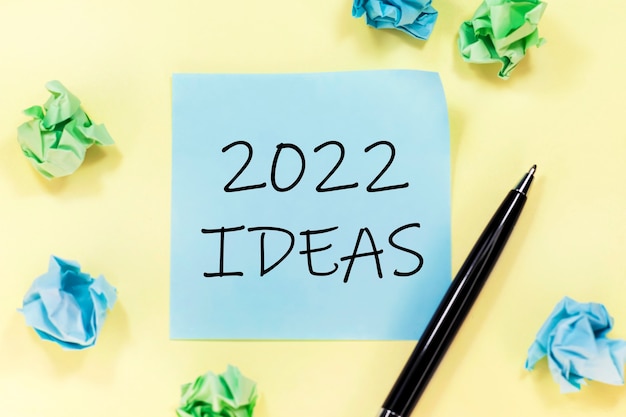 Text 2022 IDEAS on a blue sticker, black pen and pieces of paper on yellow background.