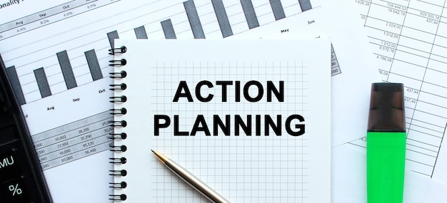 Text ACTION PLANNING on the page of a notepad lying on financial charts on the office desk