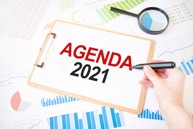 Text AGENDA 2021 on white paper sheet and marker on businessman hand on the diagram. Business concept