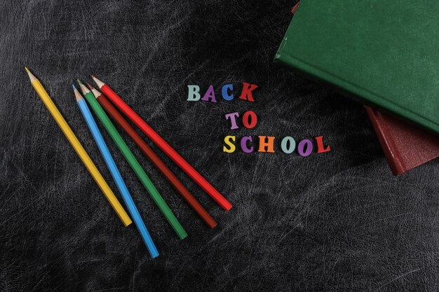 Text back to school from colored letters, books, colored pencil on a chalk board background. Top view