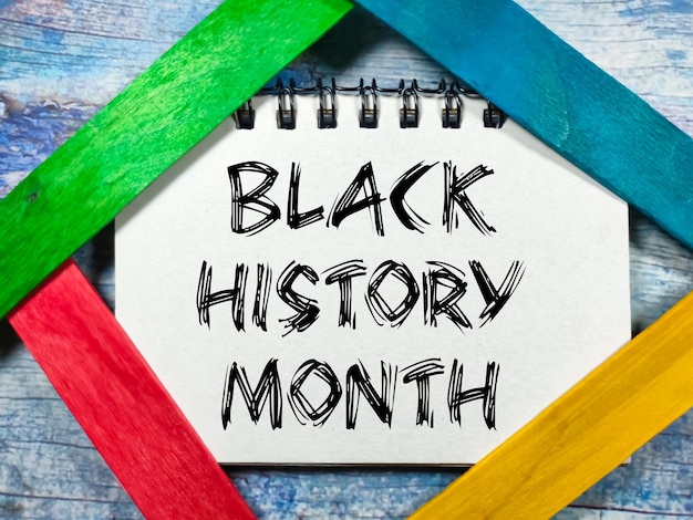 Text BLACK HISTORY MONTH writing on notebook with colored ice cream sticks on a wooden background