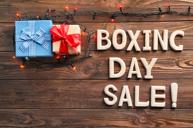 Text BOXING DAY SALE and gift boxes on wooden background