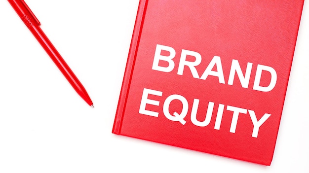 The text BRAND EQUITY is written on a red notepad near a red pen on a white table in the office Business concept