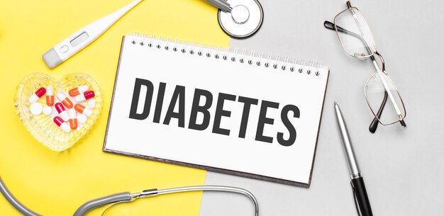 Text DIABETES on notebook with stethoscope,glasses, pen,thermometer, red pills and pen on yellow background.