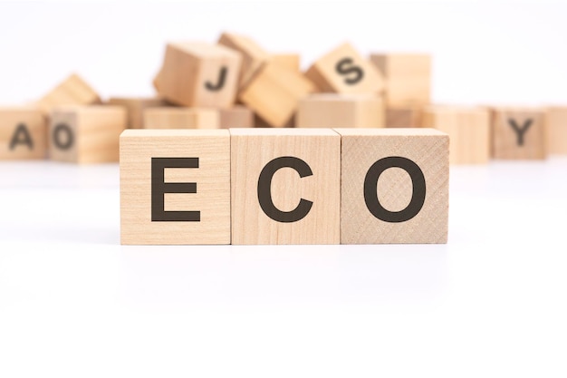 Text ECO Economic Cooperation Organisation is written on three wooden cubes standing on a white table in the background a mountain of wooden cubes with letters