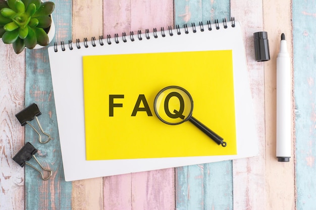 text FAQ under a magnifying glass on a yellow background top view the text is written in black marker