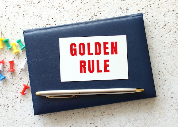 Text GOLDEN RULE on a business card lying on a blue notebook next to the pen. Business concept.