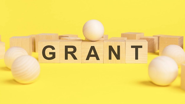 Text GRANT on wooden cubes bright yellow surface wooden sphere balls among the wood cube