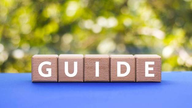 Text GUIDE on wooden cubes on blue table blurred natural background Square wood blocks Top view flat lay