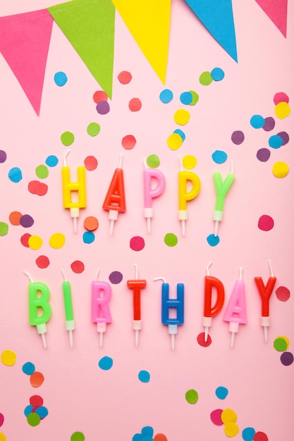 Text Happy Birthday with birthday asseccories candles and confetti on pink background Vertical photo