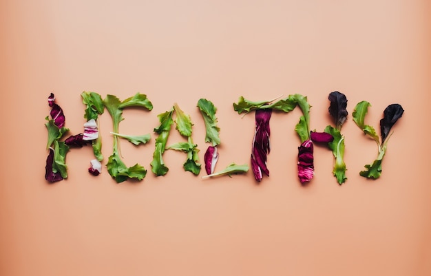 Photo text healthy using green and purple salad leafs mix on beige background. high quality photo