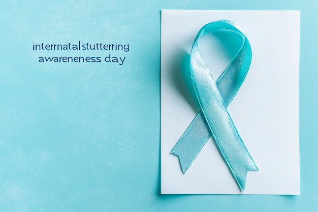 Photo the text international stuttering awareness day and an aquamarine awareness ribbon supporting those who stutter on an aquamarine background