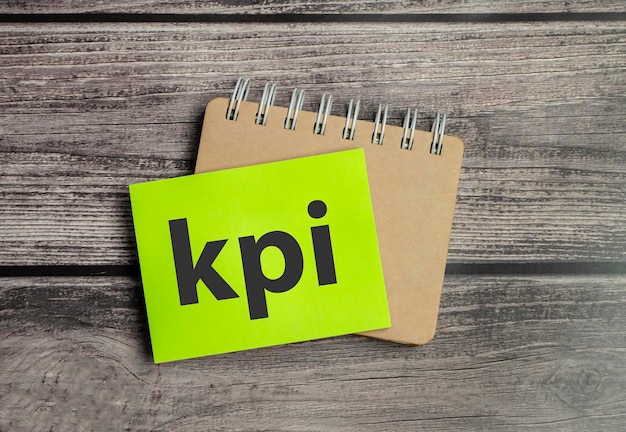 Text KPI on paper with notepad and wooden background