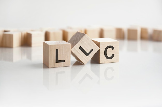 Text LLC on wooden blocks with letters on a white background reflection of the caption on the mirrored surface of the table