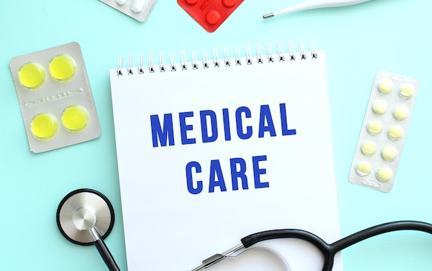 The text MEDICAL CARE is written in blue on a notebook that lies next to a stethoscope on a blue background