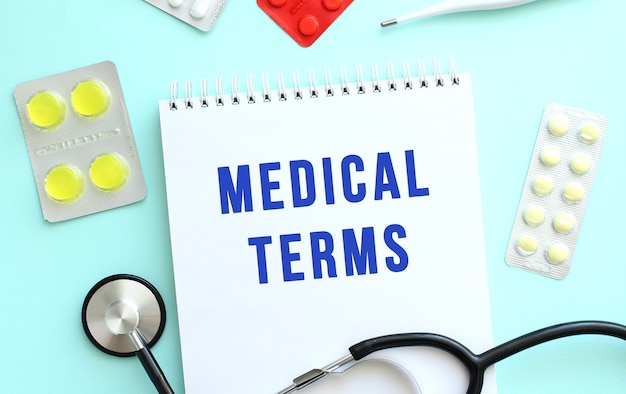 The text MEDICAL TERMS is written in a notebook that lies next to the stethoscope, medicine on a blue background.