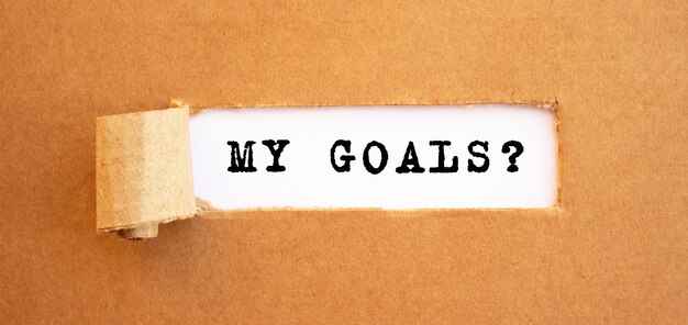 Text MY GOALS appearing behind torn brown paper. For your design, concept.