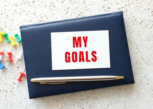 Text MY GOALS on a business card lying on a blue notebook next to the pen Business concept