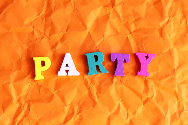 Text "Party" with colorful wooden letters on crumpled orange paper. Celebration concept