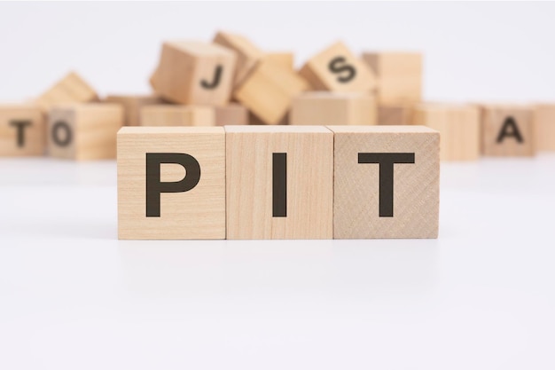 Text PIT personal income tax is written on three wooden cubes standing on a white table in the background a mountain of wooden cubes with letters