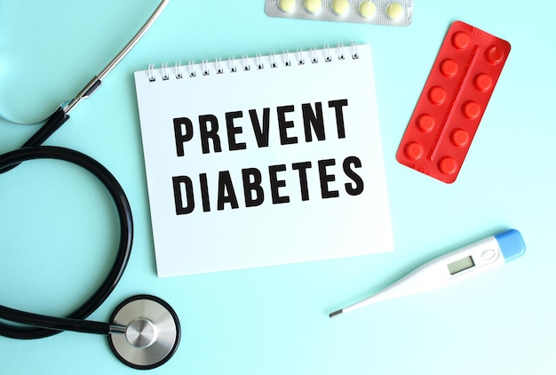 The text PREVENT DIABETES is written on a white notepad that lies next to the stethoscope and pills