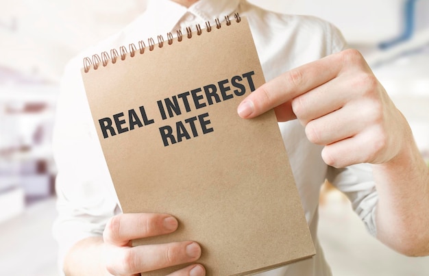 Text REAL INTEREST RATE on brown paper notepad in businessman hands in office Business concept