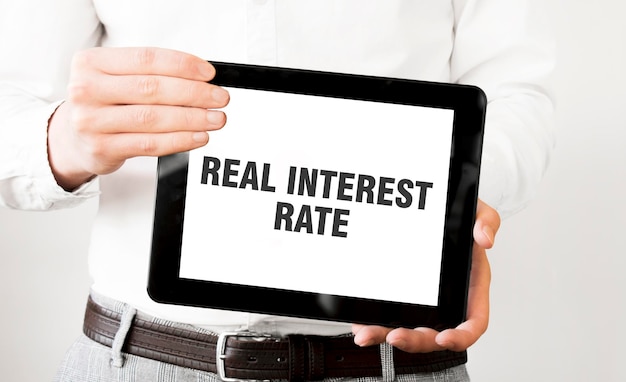 Text REAL INTEREST RATE on tablet display in businessman hands on the white background Business concept