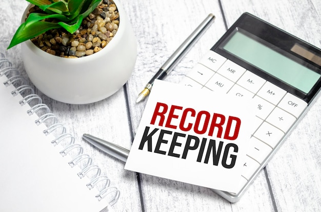 Text RECORD KEEPING on paper card and calculator on wooden background