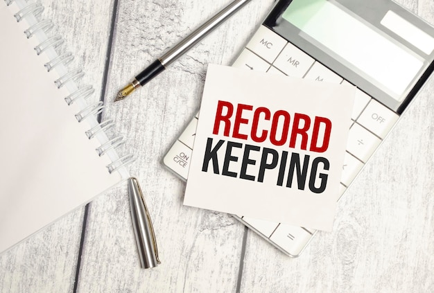 Text RECORD KEEPING on paper card and calculator on wooden background