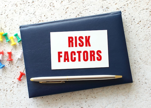 Text RISK FACTOR on a business card lying on a blue notebook next to the pen