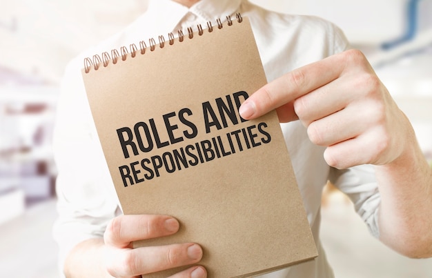 Text roles and responsibilities on brown paper notepad in businessman hands in office.