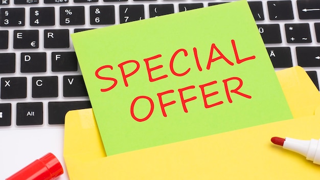 Text SPECIAL OFFER is written in red marker on a green card in the frame is a laptop keyboard on yellow notepad concept of business and finance