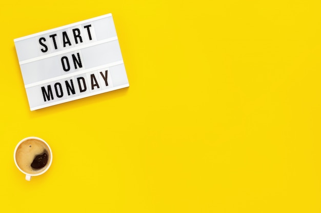 Photo text "start on monday" on lightbox and cup of coffee. start of working week. top view on yellow background.