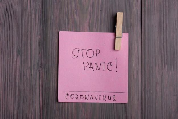 Text Stop Panic Coronavirus on sticky note that hangs with a clothespin on wooden background