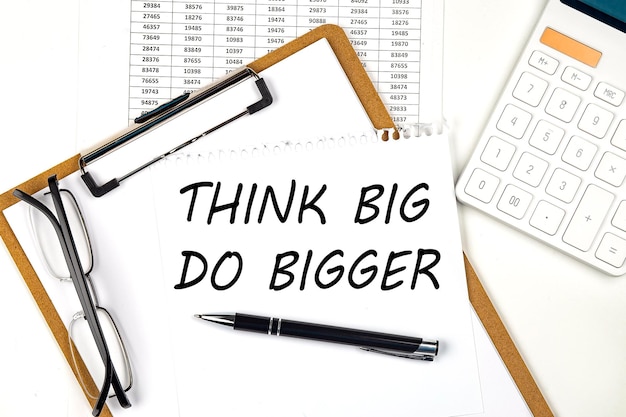 Text THINK BIG DO BIGGER on the white paper on clipboard with chart and calculator