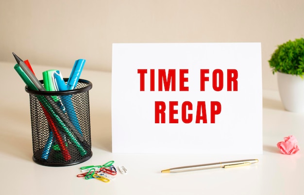 The text TIME FOR RECAP is written on a white folded sheet of paper on the table Nearby are pens and pencils