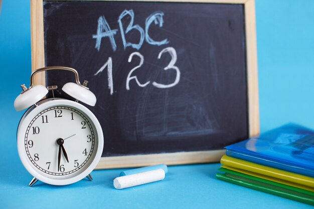 Textbooks and alarm clock with school chalkboard on a blue background