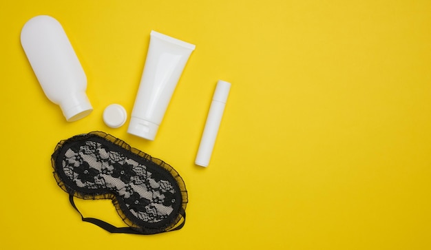 Textile sleep mask sponge and plastic tubes with cosmetics on a yellow background