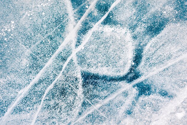 Texture of blue ice with cracks and air bubbles on the frozen lake. Macro image. Winter nature background