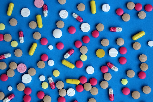 Texture of various drugs and pills scattered on a blue wall. Bright and multi-colored pills. Health and medicine theme.