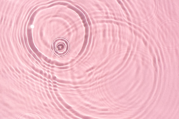 Texture wave from drops on pink water under sunlight. Top view, flat lay.