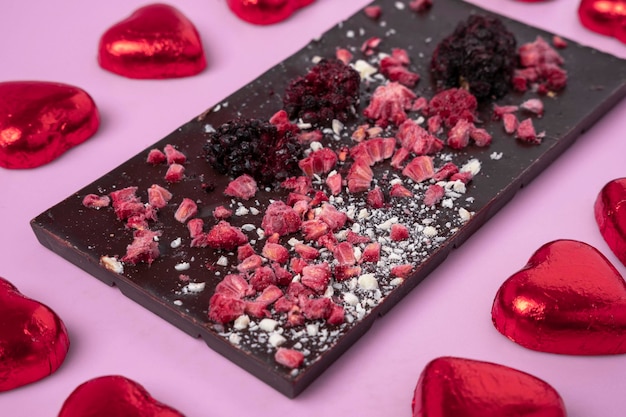 Textured background of an artistically decorated chocolate bar with berries on a pink background