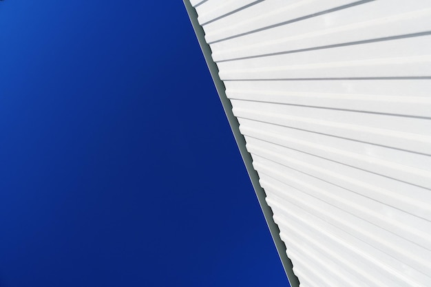 Textured white metal structures diagonally against a blue sky. Abstraction in buildings