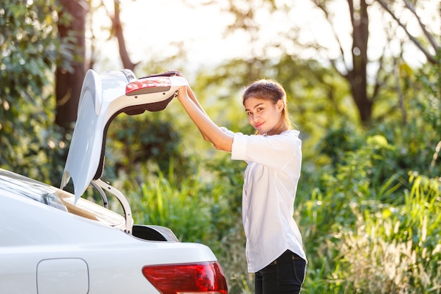 Thai asian woman smiling and standing open back of a car on the road in countryside.