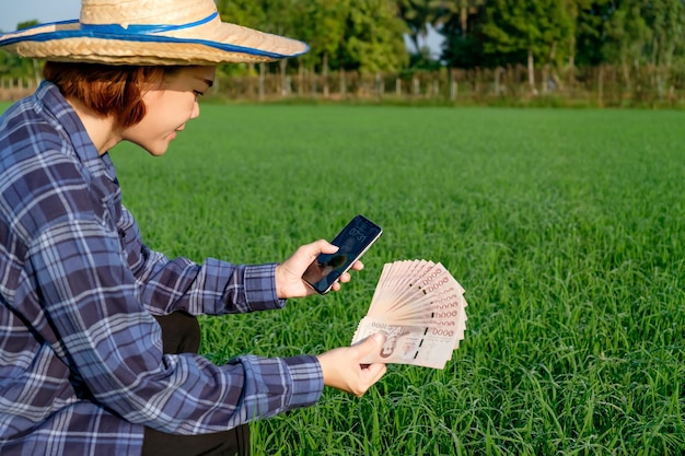 Thai banknotes money with blank screen smartphone are held by female farmers at green farms