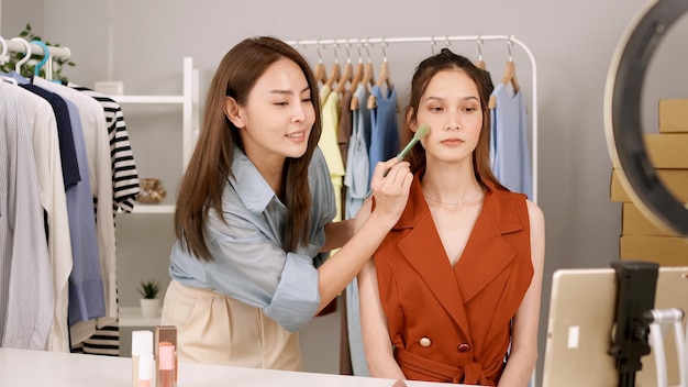 Thai beauty blogger woman live streaming cosmetics product review with Asian model. Influencer tutorial online course at home studio.