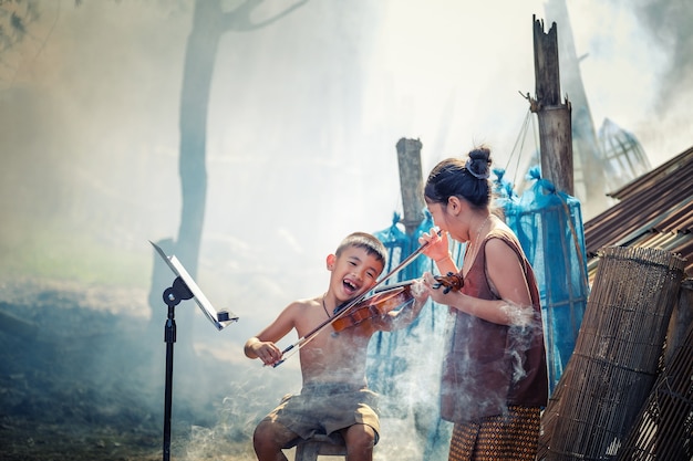 Thai boy and rural girls playing violin at her home garden.