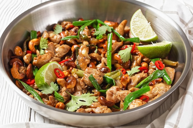 Thai cashew chicken stir fry in a pan on a wooden table horizontal view from above