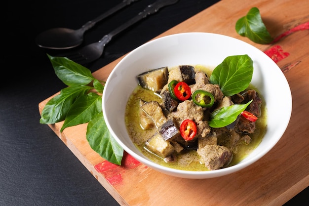 Thai Food concept homemade Thai Green curry in white ceramic bowl on wooden board and black slate stone background with copy space